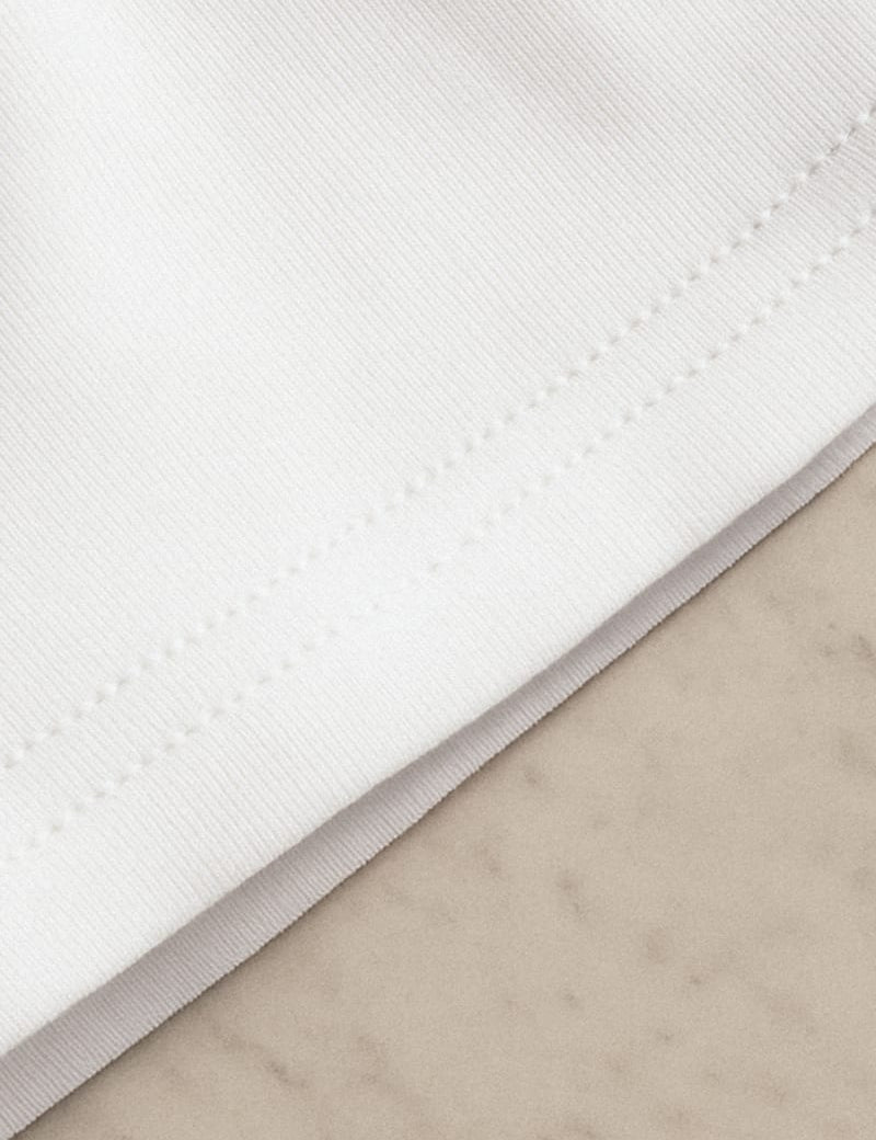 Close-up shot of an unisex oversized white t-shirt, showcasing the intricate fabric stitching,  and highlighting its premium texture and rich craftsmanship— Muselot.